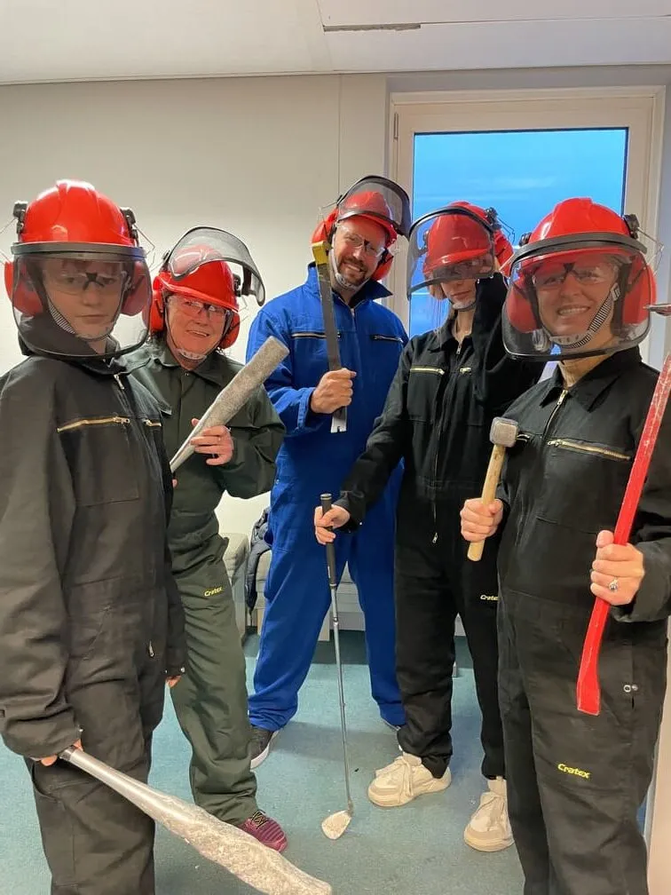 Group of people in safety gear posing with bats, crowbar, and golf club